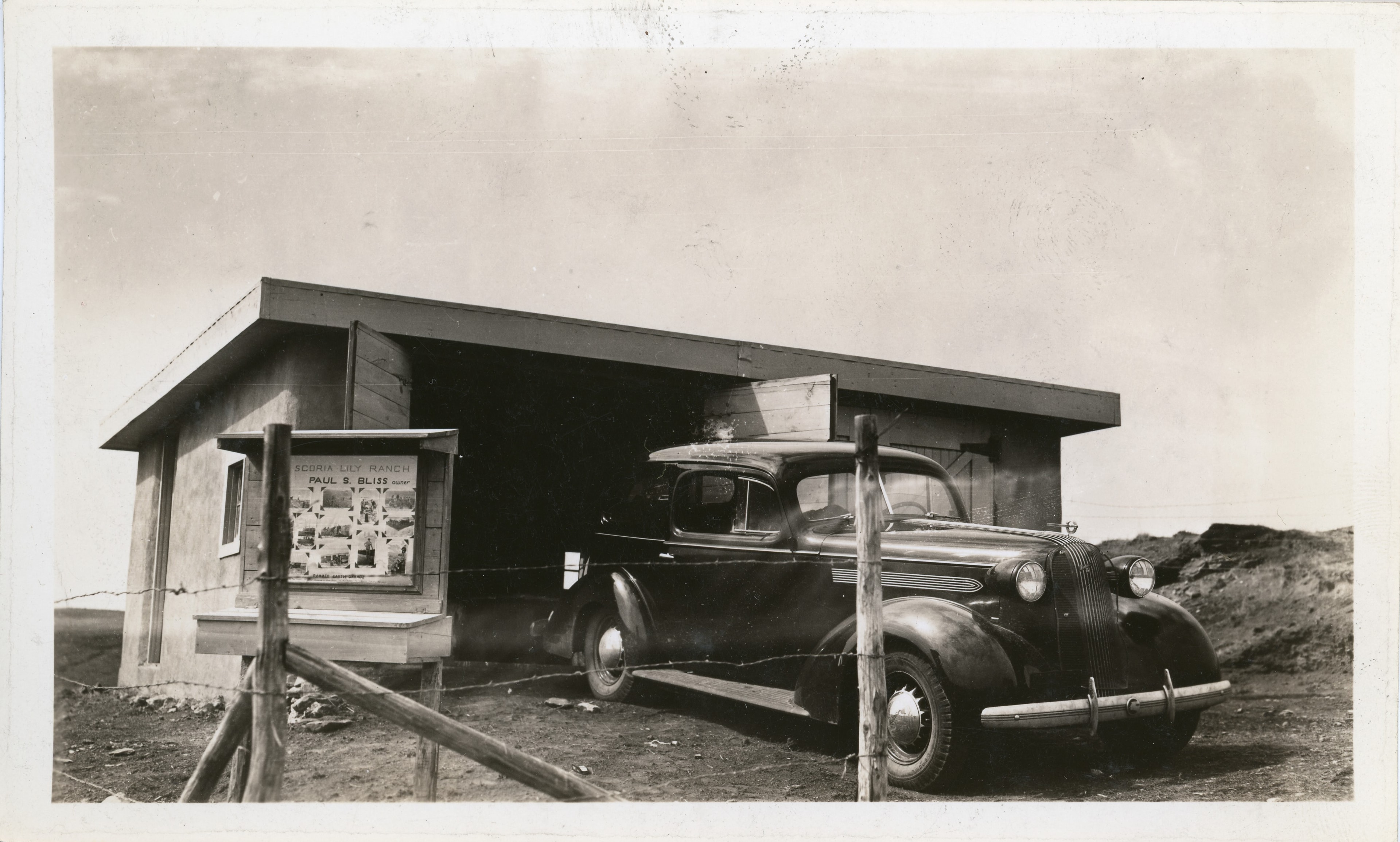Bliss's automobile parked in the rammed earth garage at Scoria Lily Ranch, with the ranch sign board visible, c. 1937