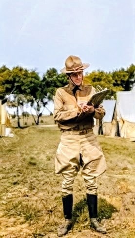Paul Southworth Bliss in military uniform at Fort Crook, writing in a notebook, with army tents in the background.